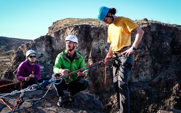 three people stand on a rocky ledge preparing to rock climb